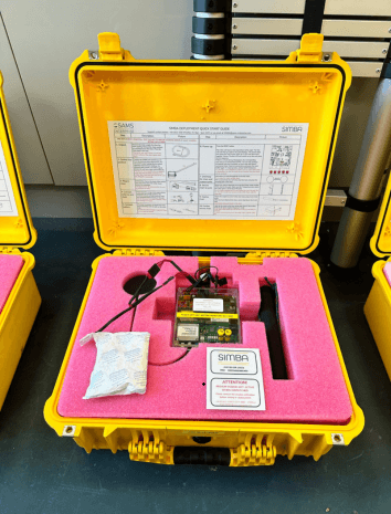 Yellow SIMBA case open to reveal snow- and ice monitoring device and accessories neatly placed in pink foam padding.